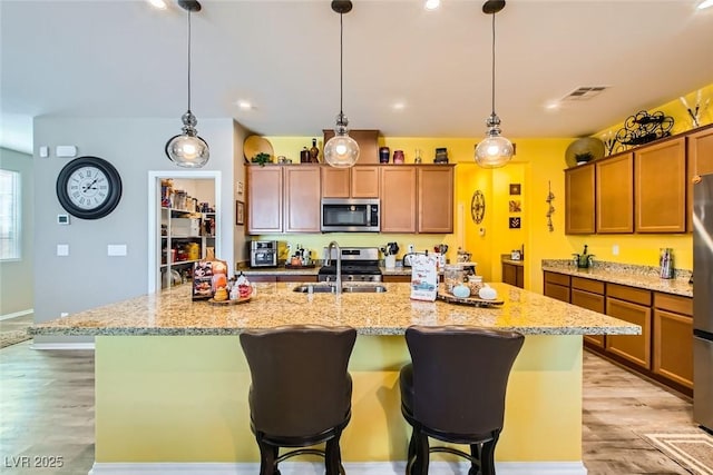 kitchen featuring stainless steel appliances, a kitchen island with sink, sink, and light wood-type flooring