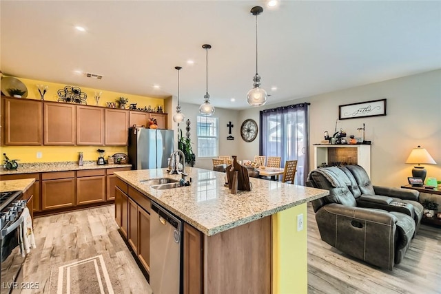 kitchen with appliances with stainless steel finishes, pendant lighting, sink, light stone counters, and a center island with sink