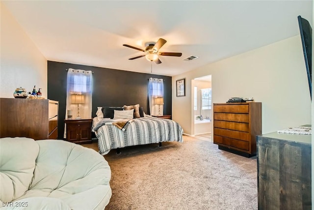 bedroom with multiple windows, ensuite bathroom, light colored carpet, and ceiling fan