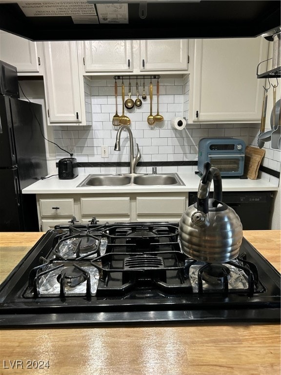 interior details with black refrigerator, tasteful backsplash, white cabinetry, and sink