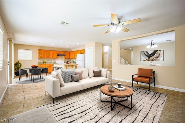 tiled living room with ceiling fan with notable chandelier