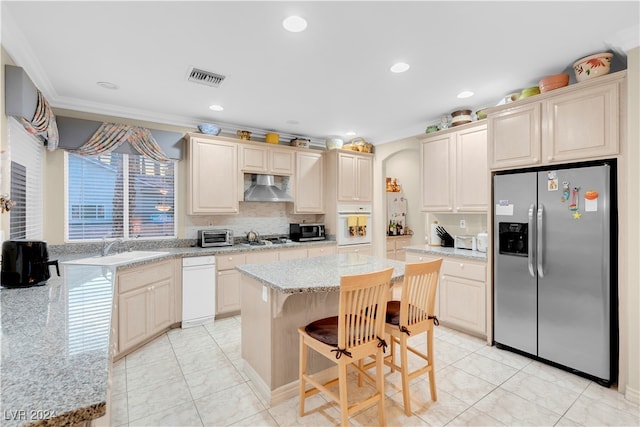 kitchen featuring appliances with stainless steel finishes, a kitchen bar, a center island, crown molding, and light stone counters