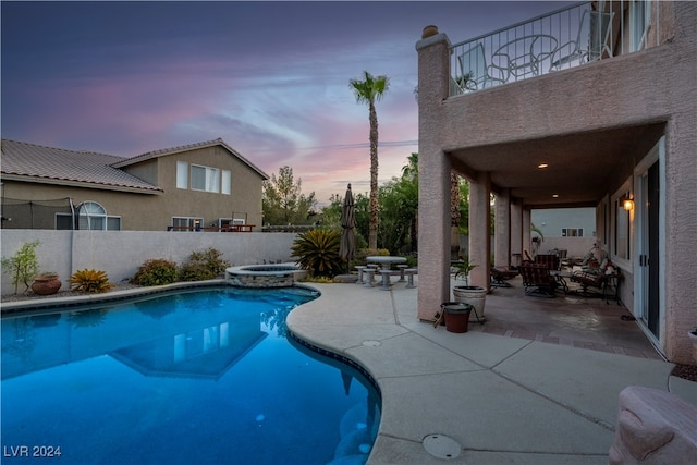 pool at dusk featuring an in ground hot tub and a patio