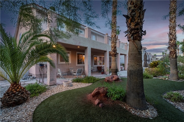 back house at dusk with a patio area and a yard