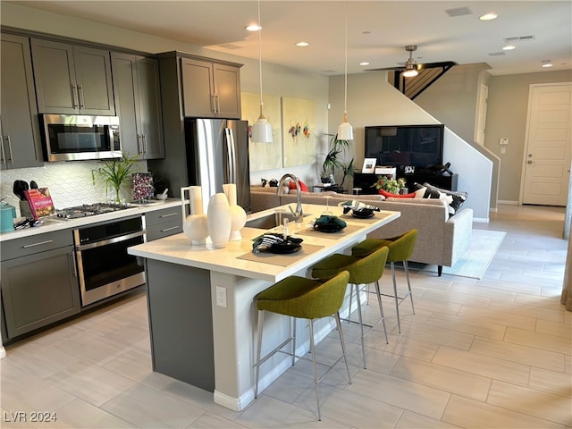 kitchen featuring gray cabinets, sink, an island with sink, a kitchen breakfast bar, and stainless steel appliances