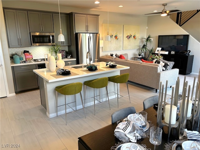 kitchen with a kitchen breakfast bar, gray cabinetry, a kitchen island with sink, and stainless steel appliances