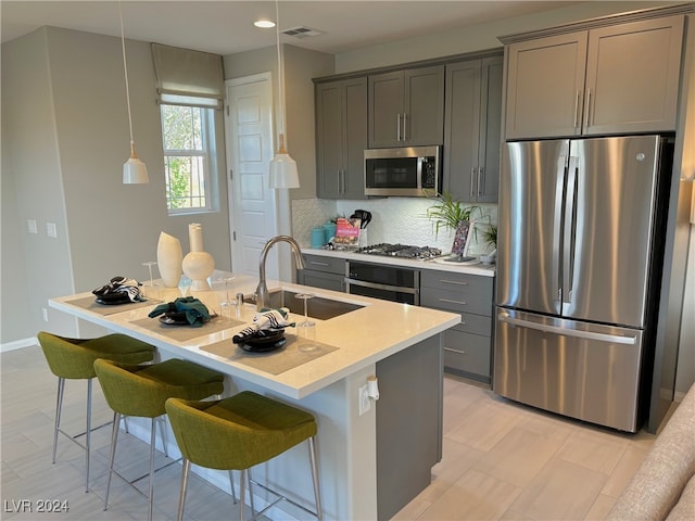 kitchen featuring a center island with sink, stainless steel appliances, sink, and gray cabinetry