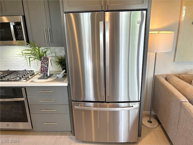 kitchen with appliances with stainless steel finishes, decorative backsplash, gray cabinetry, and light tile patterned floors