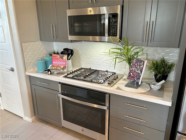 kitchen with light tile patterned flooring, appliances with stainless steel finishes, tasteful backsplash, and gray cabinetry