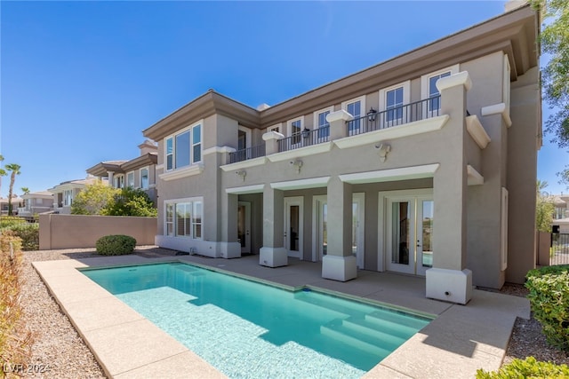 rear view of property featuring a balcony, a fenced in pool, and a patio area