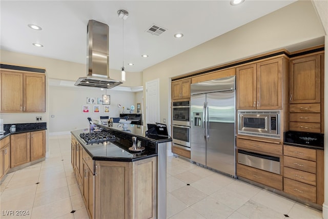 kitchen with a kitchen island, dark stone countertops, island range hood, built in appliances, and light tile patterned floors