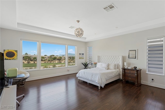 bedroom with an inviting chandelier, a tray ceiling, and dark hardwood / wood-style flooring