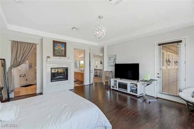 bedroom with dark wood-type flooring, a tray ceiling, an inviting chandelier, ensuite bathroom, and a multi sided fireplace