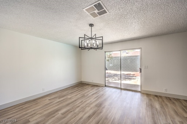 unfurnished room featuring a textured ceiling, wood-type flooring, and an inviting chandelier