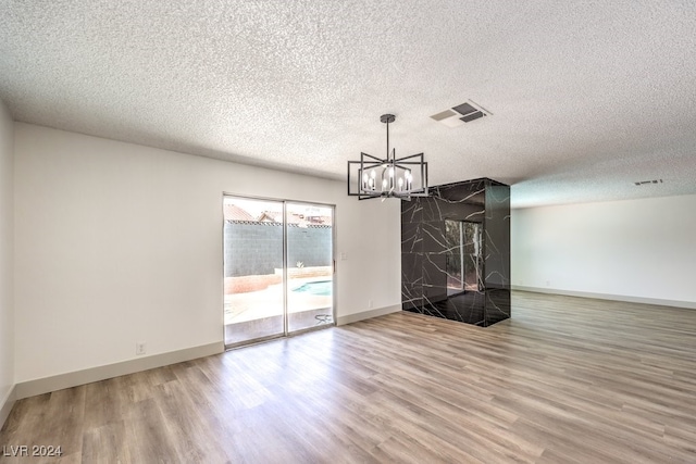 unfurnished living room with a textured ceiling, an inviting chandelier, a large fireplace, and hardwood / wood-style flooring