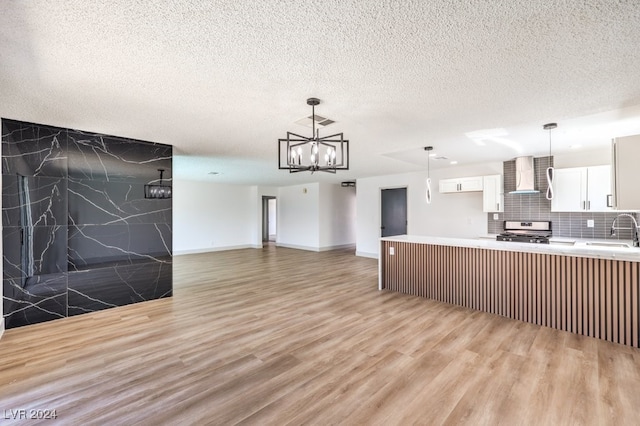 kitchen with light wood-type flooring, wall chimney range hood, stainless steel stove, and white cabinets