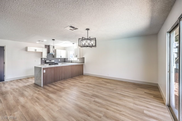 kitchen featuring light wood-type flooring, stainless steel range oven, white cabinets, kitchen peninsula, and wall chimney range hood