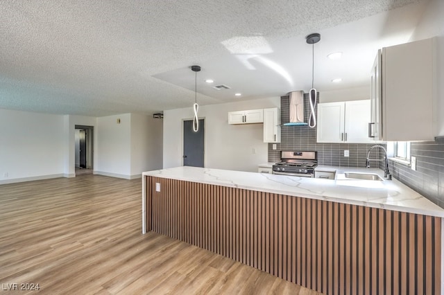 kitchen featuring white cabinets, kitchen peninsula, light wood-type flooring, stainless steel range with gas stovetop, and sink