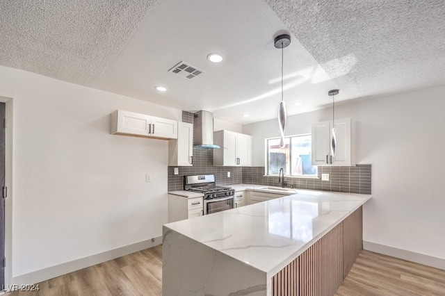 kitchen with white cabinets, kitchen peninsula, pendant lighting, gas stove, and wall chimney range hood