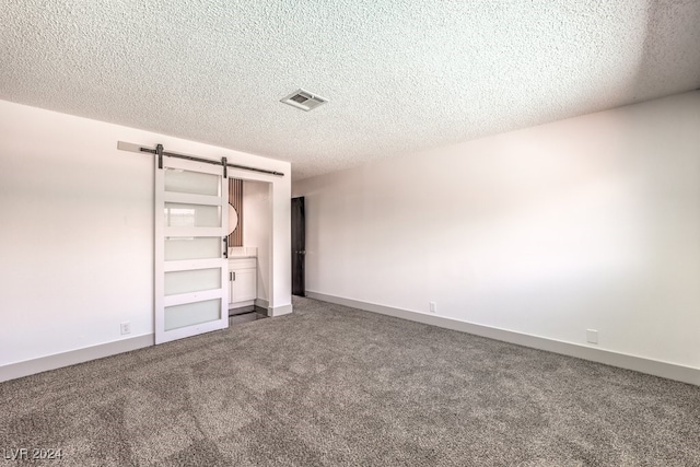 unfurnished bedroom with a textured ceiling, a barn door, and carpet