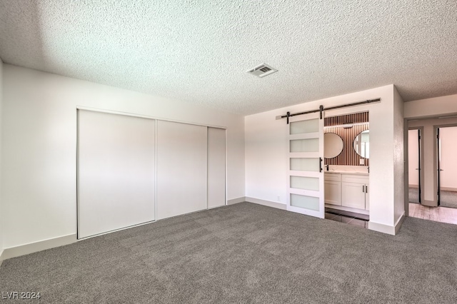 unfurnished bedroom with a barn door, a textured ceiling, dark carpet, and a closet