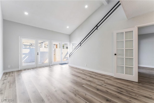 unfurnished living room featuring french doors, light hardwood / wood-style floors, and high vaulted ceiling