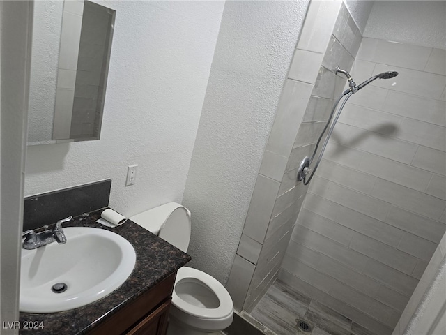 bathroom featuring tiled shower, toilet, and vanity