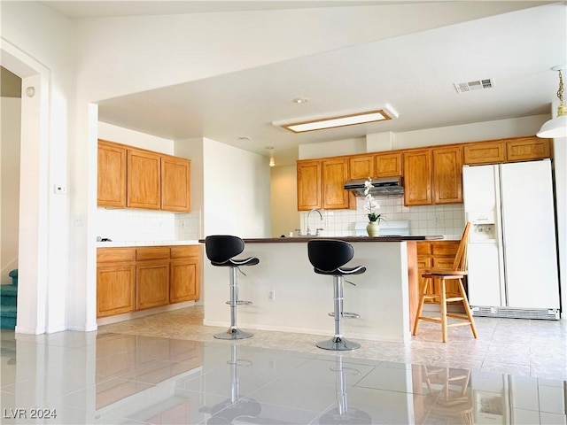 kitchen featuring light tile patterned floors, under cabinet range hood, a breakfast bar, visible vents, and white fridge with ice dispenser
