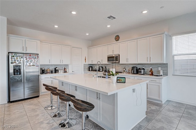 kitchen with tasteful backsplash, stainless steel appliances, a breakfast bar, a center island with sink, and white cabinets