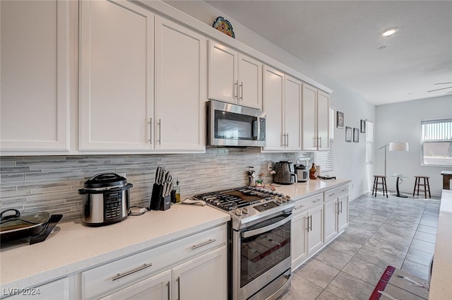 kitchen featuring white cabinets, appliances with stainless steel finishes, backsplash, and light tile patterned flooring