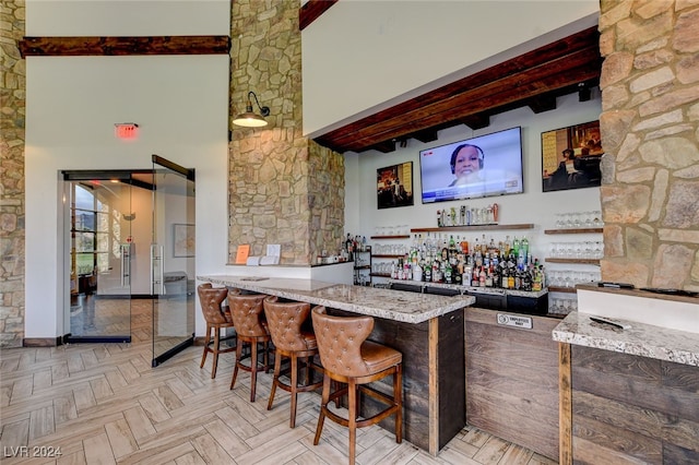 bar with a towering ceiling, light parquet floors, and beamed ceiling