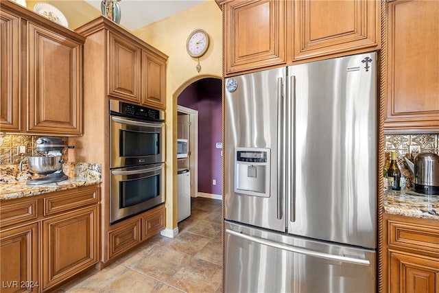 kitchen with backsplash, light stone countertops, and appliances with stainless steel finishes