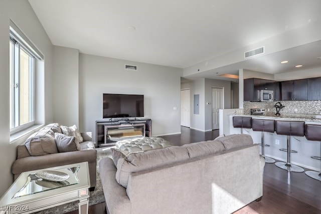 living area featuring baseboards, dark wood finished floors, visible vents, and electric panel