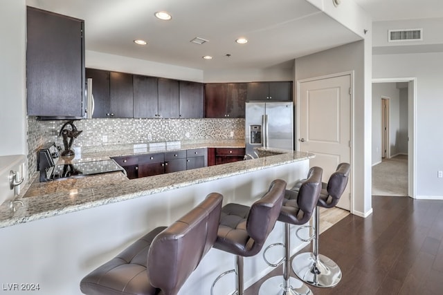 kitchen featuring stove, dark brown cabinetry, kitchen peninsula, stainless steel refrigerator with ice dispenser, and light stone countertops