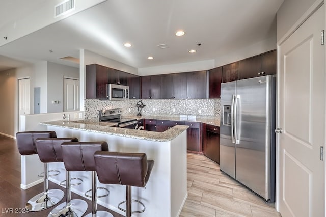 kitchen with dark brown cabinetry, a breakfast bar, tasteful backsplash, appliances with stainless steel finishes, and kitchen peninsula