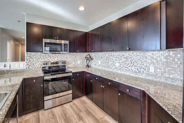 kitchen with stainless steel appliances, backsplash, dark brown cabinets, and light stone countertops