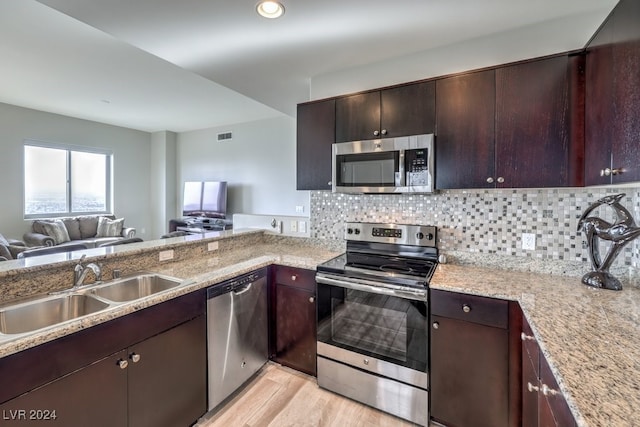 kitchen featuring a sink, open floor plan, appliances with stainless steel finishes, light wood-type flooring, and tasteful backsplash