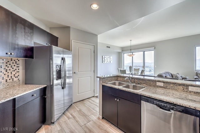 kitchen with decorative light fixtures, stainless steel appliances, tasteful backsplash, open floor plan, and a sink