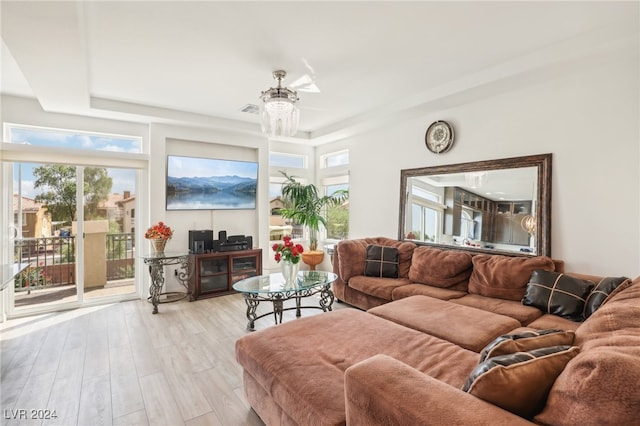 living room featuring light hardwood / wood-style floors, a wealth of natural light, a notable chandelier, and a tray ceiling