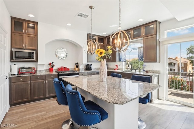 kitchen featuring stainless steel microwave, an inviting chandelier, a kitchen island, light stone countertops, and light hardwood / wood-style floors