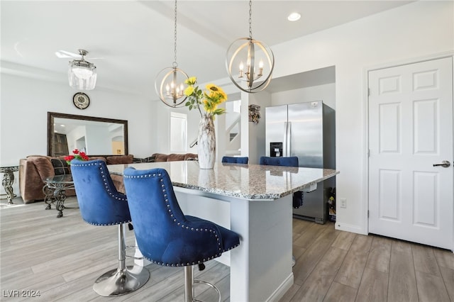 kitchen with pendant lighting, a breakfast bar, stainless steel refrigerator with ice dispenser, and light hardwood / wood-style flooring