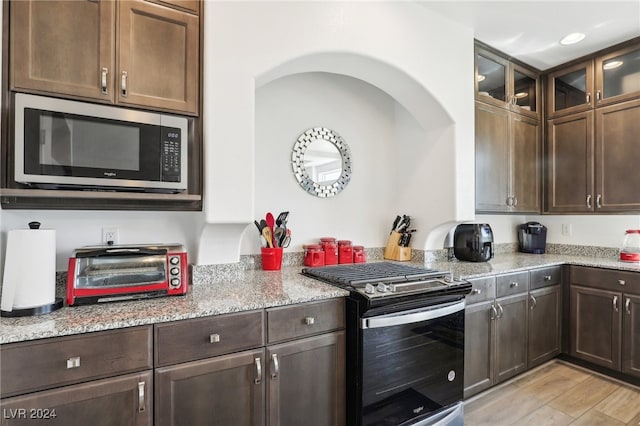 kitchen with dark brown cabinetry, stainless steel appliances, light hardwood / wood-style flooring, and light stone counters