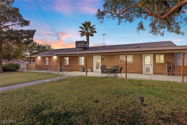 back house at dusk featuring a yard, a patio, and central air condition unit