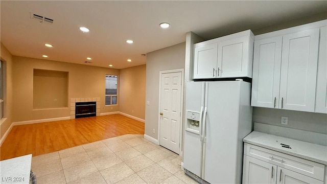 kitchen with white cabinetry, white refrigerator with ice dispenser, a tile fireplace, and light hardwood / wood-style flooring