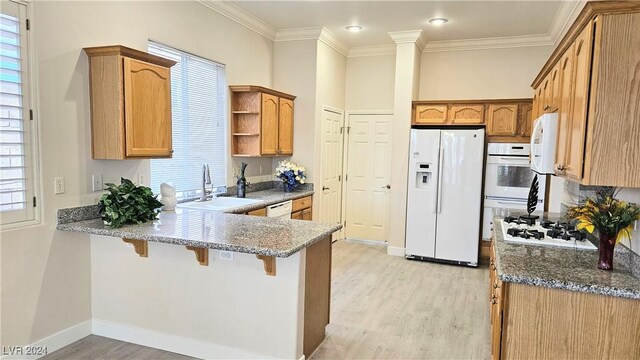 kitchen with a peninsula, white appliances, a sink, and light wood-style flooring