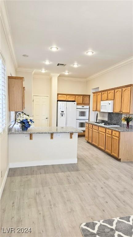 kitchen with light stone counters, a breakfast bar, visible vents, white appliances, and a peninsula