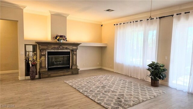 living area with a glass covered fireplace, ornamental molding, wood finished floors, and visible vents