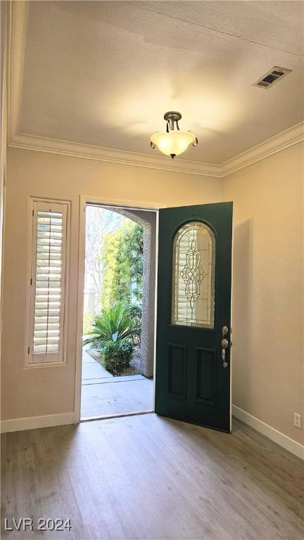 entrance foyer featuring ornamental molding, visible vents, baseboards, and wood finished floors