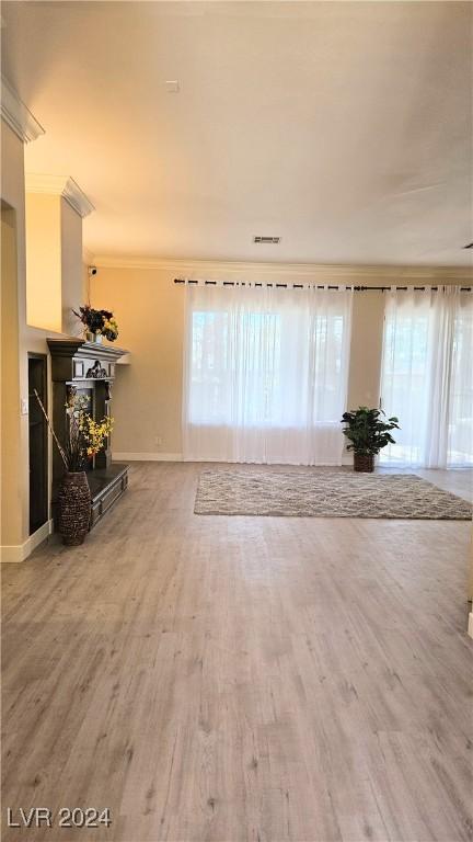 unfurnished living room featuring visible vents, a fireplace with raised hearth, ornamental molding, wood finished floors, and baseboards