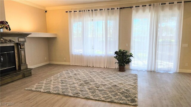 unfurnished living room featuring baseboards, ornamental molding, wood finished floors, and a glass covered fireplace